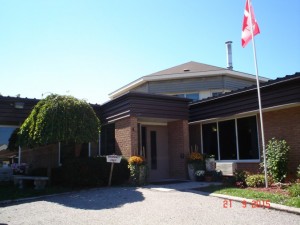 Front entrance of two story building with greenery and Canadian flag